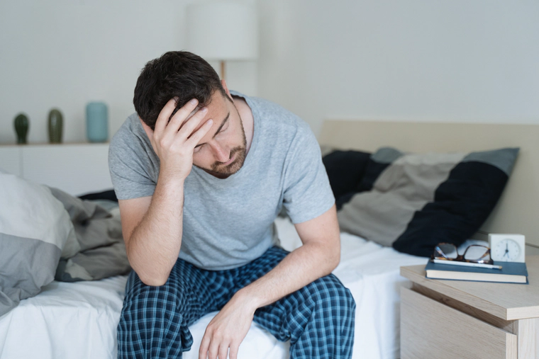 Man did not slept well, sits on a bed