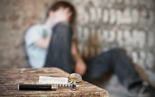 Addict in background, foreground focused on heroin paraphernalia